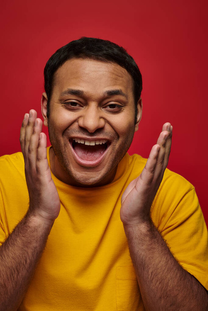 kasvot ilme, innoissaan intialainen mies keltainen t-paita elehtii punaisella pohjalla, avoin suu - Valokuva, kuva