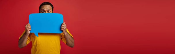 indian man with eyes wide open hiding behind blank speech bubble on red background, emotion, banner - Photo, Image