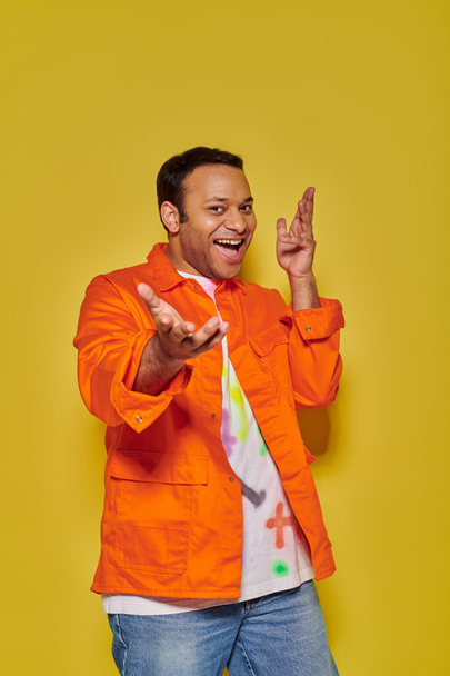 muotokuva innoissaan intialainen mies oranssi takki ja diy t-paita ele keltainen tausta - Valokuva, kuva