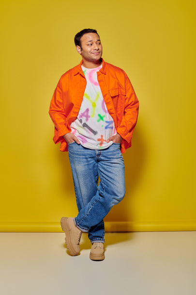 piena lunghezza di elegante uomo indiano in giacca arancione e giacca di jeans in posa su sfondo giallo - Foto, immagini