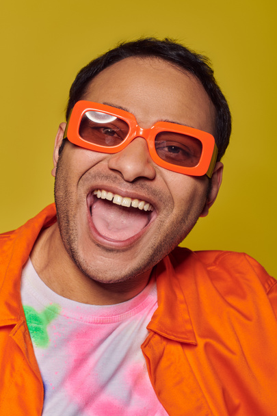 self-expression concept, excited indian man in orange sunglasses smiling on yellow backdrop - Photo, Image