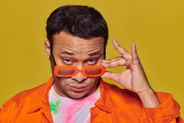 conceito de auto-expressão, homem indiano confiante ajustando óculos de sol laranja no fundo amarelo - Foto, Imagem