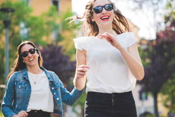 Kaksi nuorta naista Millennials ulkona kaupungissa käynnissä ja hyppääminen hauskaa hymyillen - Valokuva, kuva