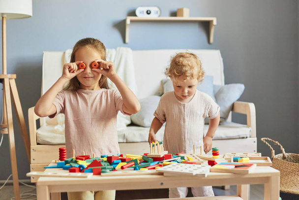 Playful preschooler activities. Infant's adorable playtime. Happy girls sisters having fun together with wooden educational  toys playing together at homer interior. - Photo, Image