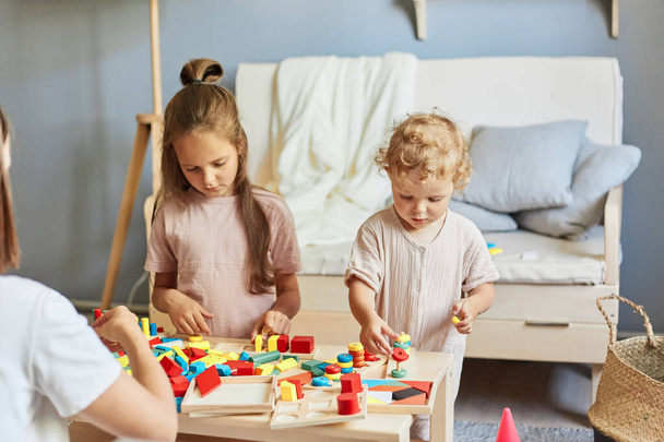 Studying through play and toys. Smart educational lesson. Concentrated girls sisters learning together with wooden educational  toys playing together at homer interior. - Φωτογραφία, εικόνα
