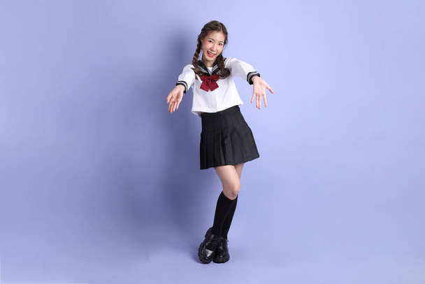 Азиатка в японской студенческой форме стоит на фиолетовом фоне. - Фото, изображение