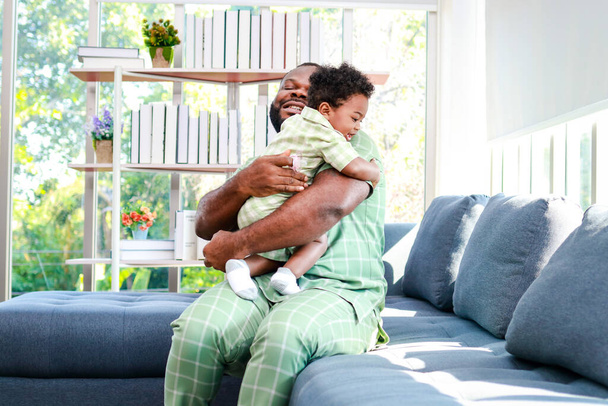 Vader die zijn zoontje in zijn armen hield Ze glimlachten gelukkig in de woonkamer thuis. Afrikaans amerikaanse familie thuis - Foto, afbeelding