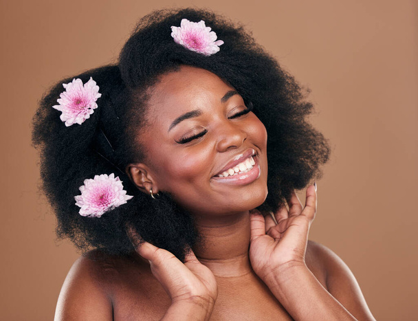Afro, hair or happy black woman with flowers, beauty care or smile on a brown studio background. Hairstyle, floral or natural African female model with shine or growth with volume, wellness or glow. - Φωτογραφία, εικόνα