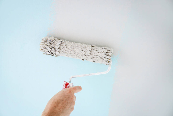 Человек работает с помощью рулона краски, чтобы перекрасить старые стены краски, прокатки инструмент. Синий до нейтрального. Дом в помещении. - Фото, изображение