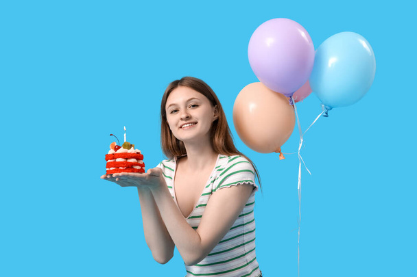 Hübsche junge Frau mit Geburtstagstorte und Luftballons auf blauem Hintergrund - Foto, Bild