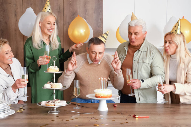 Kypsä mies ystäviensä kanssa tekee toiveen syntymäpäiväjuhliin keittiössä - Valokuva, kuva