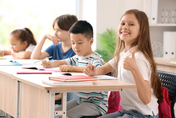 Маленькая школьница показывает большой палец вверх во время урока в классе - Фото, изображение
