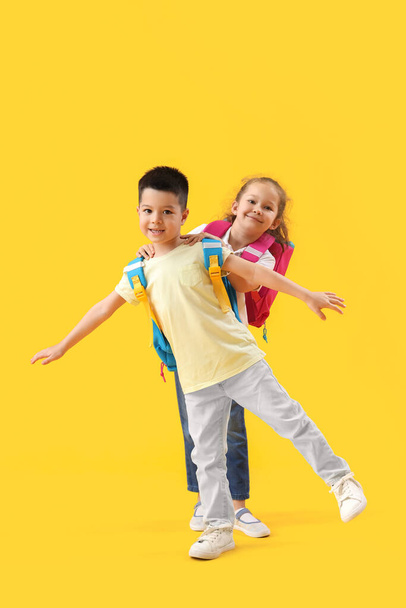 Niedliche kleine Schüler mit Rucksäcken auf gelbem Hintergrund - Foto, Bild