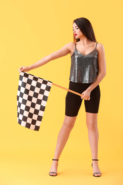 Beautiful young woman with racing flag on yellow background - Photo, Image