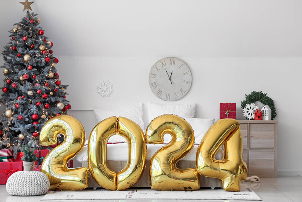 Balloons in shape of figure 2024 near comfortable bed in bedroom with Christmas decor - Photo, Image