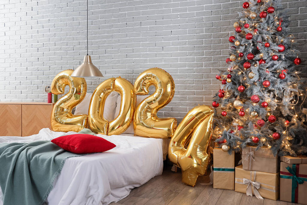 Luftballons in Form der Figur 2024 auf bequemem Bett im festlichen Schlafzimmer mit Weihnachtsdekor - Foto, Bild