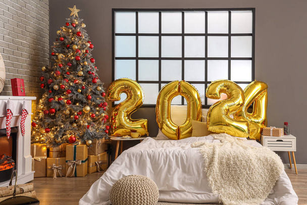 Balloons in shape of figure 2024 on comfortable bed in festive bedroom with Christmas decor - Photo, Image