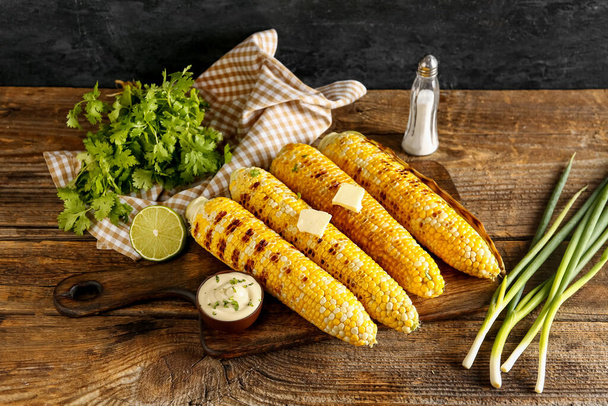 Tabla de sabrosas mazorcas de maíz a la parrilla con mantequilla y perejil sobre mesa de madera - Foto, Imagen