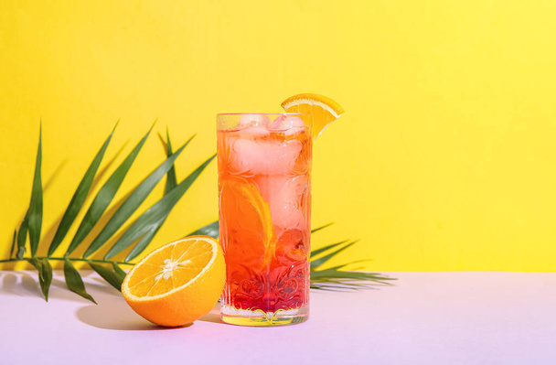Glass of tasty Negroni cocktail, orange and palm leaf on color background - Photo, Image