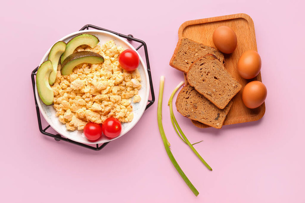Plate of tasty scrambled eggs with avocado and tomatoes on pink background - Photo, Image