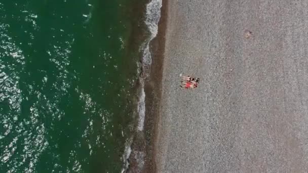 Légi felvétel néhány emberről a kavicsos parton. Szabadidős Kaland. Drone lő hullámok tenger és repül körül pár szerelmes a nászútjukon.Meet or Lovers. Lazíts az óceánon. Zöld tenger és kövek. - Felvétel, videó