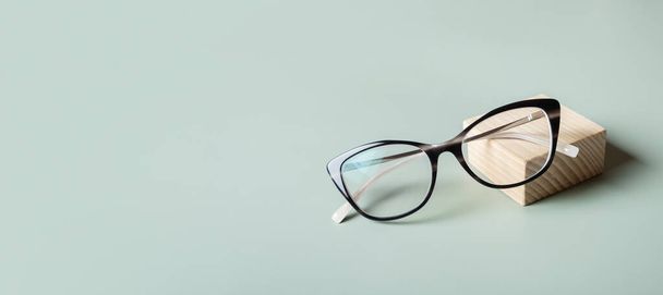 コピースペース付きのパステルグリーンバナーの背景に眼鏡をかけたポディウム. 光学店,ビジョンテスト,スタイリッシュなメガネコンセプト - 写真・画像