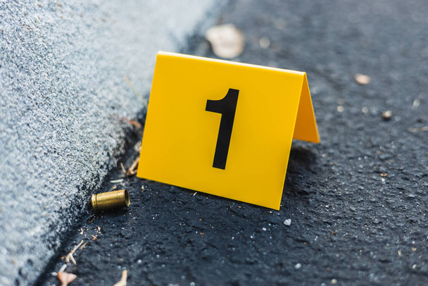 One yellow crime scene evidence marker on the street after a gun shooting brass bullet shell casing 9mm handgun pistol - Photo, Image
