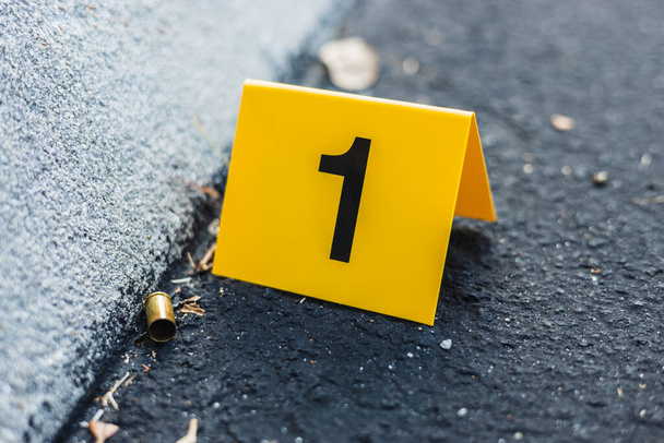 Een gele misdaad bewijs marker op straat na een pistool schieten messing kogelhuls 9mm pistool pistool - Foto, afbeelding