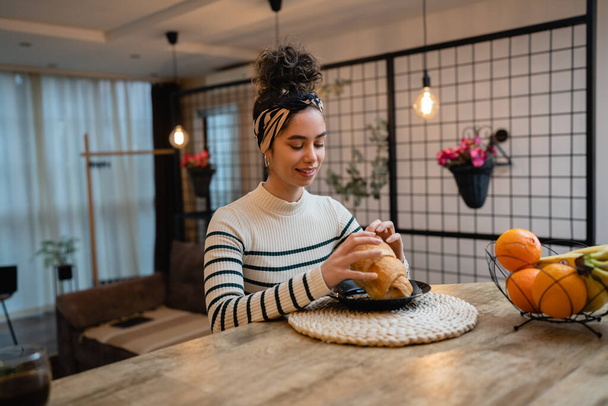 one woman beautiful young female sit at the kitchen table in the morning happy smile having croissant and cup of coffee for breakfast real people copy space daily routine concept - Photo, image
