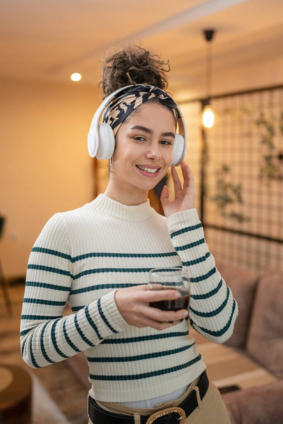yksi nainen muotokuva valkoihoinen nuori nainen seisoo kotona kuppi kahvia ja kuulokkeet kotona onnellinen hymy luottavainen oikeita ihmisiä kopioida tilaa - Valokuva, kuva