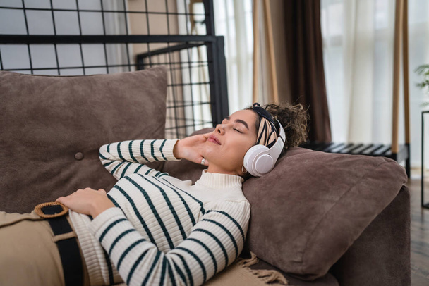 one woman adult caucasian female millennial using headphones for online guided meditation practicing mindfulness yoga with eyes closed on the bed at home real people self care concept copy space - Photo, Image