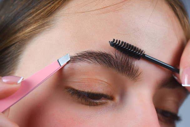 Eyebrows shape. Close up of woman getting eyebrow make-up. Macro applying cosmetics on her eyebrow with brush. Perfect shape of eyebrow, brown eyeshadows and long eyelashes. Shape eyebrows - Fotoğraf, Görsel