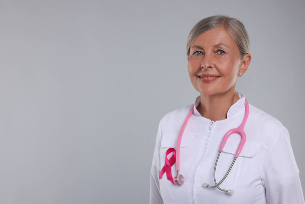 Doctor with pink ribbon and stethoscope on light grey background, space for text. Breast cancer awareness - Fotografie, Obrázek