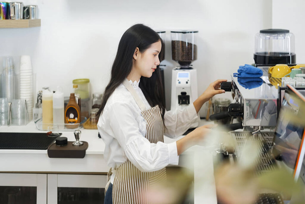 Молодой веселый бариста в фартуке во время приготовления кофе в автомате в современной кофейне. Концепция собственности. - Фото, изображение