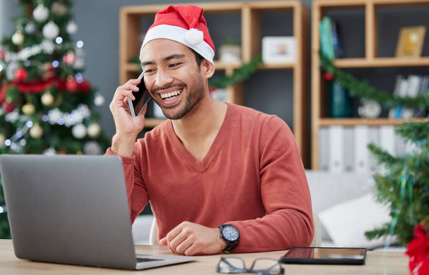 Telefonhívás, karácsonyi kalap és üzletember az irodában egy laptoppal a mobilján, hogy kommunikáljanak. Boldog, mosolygós és férfi kreatív alkalmazott a munkahelyi mobilbeszélgetések karácsonyi dekorációjával. - Fotó, kép