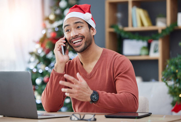 Telefonhívás, karácsonyi kalap és férfi az irodában egy laptoppal a mobilján, hogy kommunikáljanak. Boldog, mosolygós és fiatal férfi kreatív tervező xmas dekorációk mobil beszélgetés a munkahelyen. - Fotó, kép