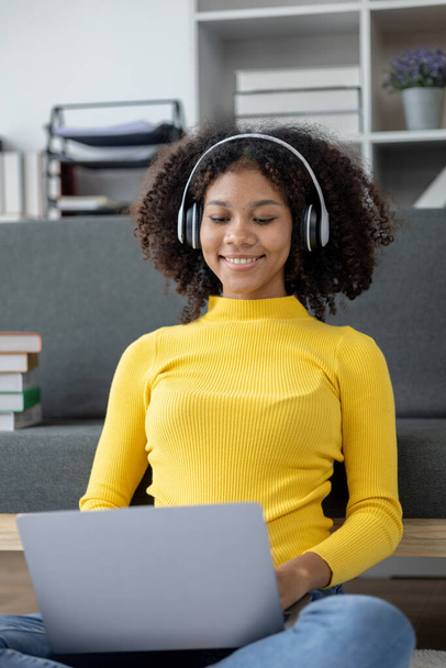 American woman sits in living room on weekends, she is wearing headphones listening to music and spending her days off social media watching movies and listening to music. Holiday activities concept. - Photo, Image
