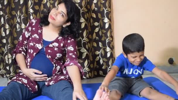 Schwangere beim Schwangerschafts-Yoga posiert bequem zu Hause mit ihrem Kind, Schwangere übt zu Hause mit ihrem Sohn einfache Yogaschritte, Schwangerschafts-Yoga und Fitness-Posen - Filmmaterial, Video