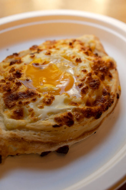 Cocina georgiana tradicional. Ajara Khachapuri en placa de papel. Lleno de queso y cubierto con huevo crudo y mantequilla, pan relleno de queso. Deliciosa comida - Foto, imagen