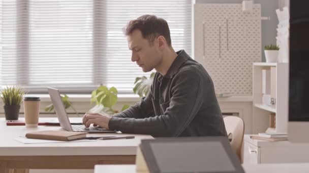 Side view slowmo του επικεντρώθηκε Καυκάσιος επιχειρηματίας που εργάζονται σε φορητό υπολογιστή κάθεται στο γραφείο στο γραφείο - Πλάνα, βίντεο