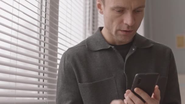 Slowmo όμορφος Καυκάσιος επιχειρηματίας κοιτάζοντας μέσα από το παράθυρο τυφλή, ενώ κάνοντας ένα τηλεφώνημα - Πλάνα, βίντεο
