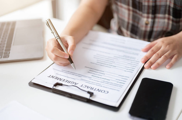 Close-up image of a woman signing her signature on a contract agreement at a table. legal, financial contract, paperwork - Photo, Image