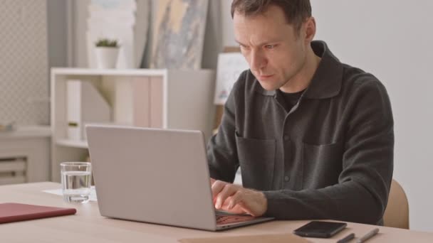 Harkitsevainen valkoihoinen liikemies kirjoittaa kannettavaan tietokoneeseen työskennellessään virassa olevan rahoitusprojektin parissa - Materiaali, video