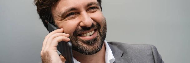 Smiling mid aged businessman talking on mobile phone over gray wall background outdoors - Photo, image