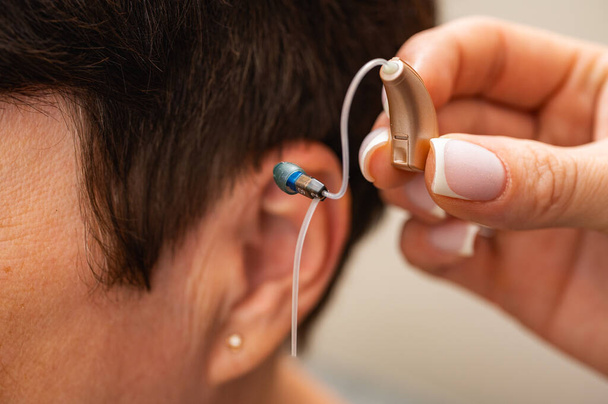 Een vrouw past een gehoorapparaat verborgen in haar oor op een lichte achtergrond. Herstel van het gehoor. Technische middelen - Foto, afbeelding
