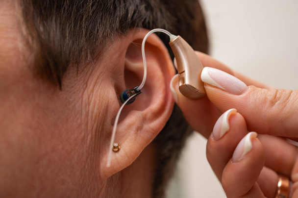 Una mujer se prueba un audífono escondido en su oído sobre un fondo claro. Restauración del oído. Medios técnicos - Foto, imagen