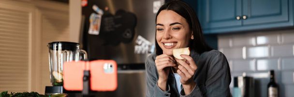 Smiling woman taking selfie footage with apple on cellphone at home kitchen - Valokuva, kuva