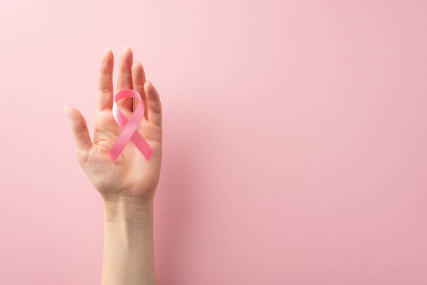 Faites entendre votre voix en ce Mois international de la sensibilisation au cancer du sein. Photo vue du dessus des mains de la femme tenant un ruban rose sur fond rose pastel, offrant un copyspace pour le texte ou la publicité - Photo, image