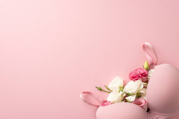 Representación de la conciencia del cáncer de mama: Vista superior de un sujetador lleno de elegantes flores de eustoma sobre un fondo rosa suave. Espacio adecuado para el texto o el contenido promocional - Foto, Imagen