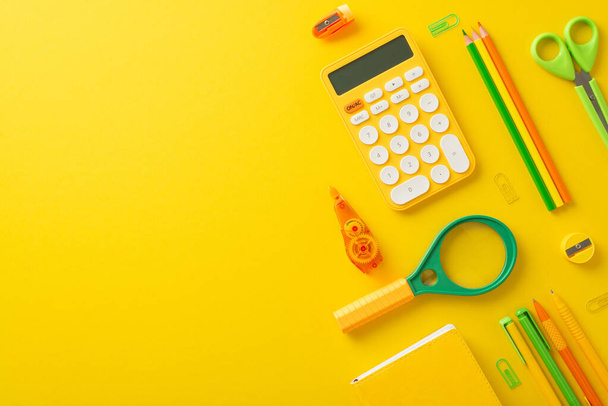 Enhance productivity with this student's study setup. Top view image of calculator and other stationery on bright yellow isolated background, providing ample copy-space for text or advertising - Photo, Image